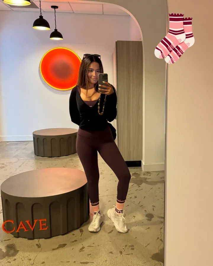 A mirror selfie in a studio lobby wearing raspberry and cream striped grip socks with sneakers