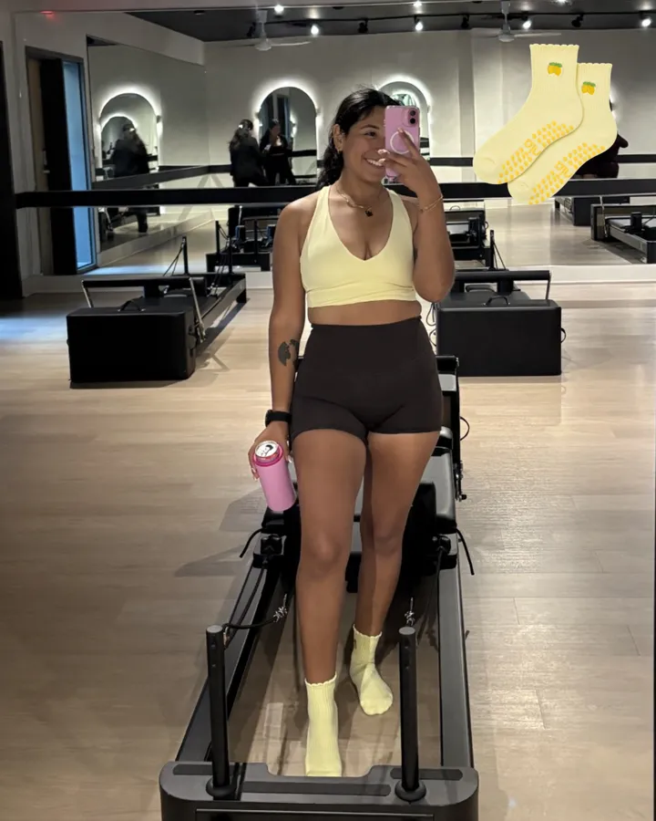 A smiling mirror selfie on a reformer in yellow Lemon grip socks